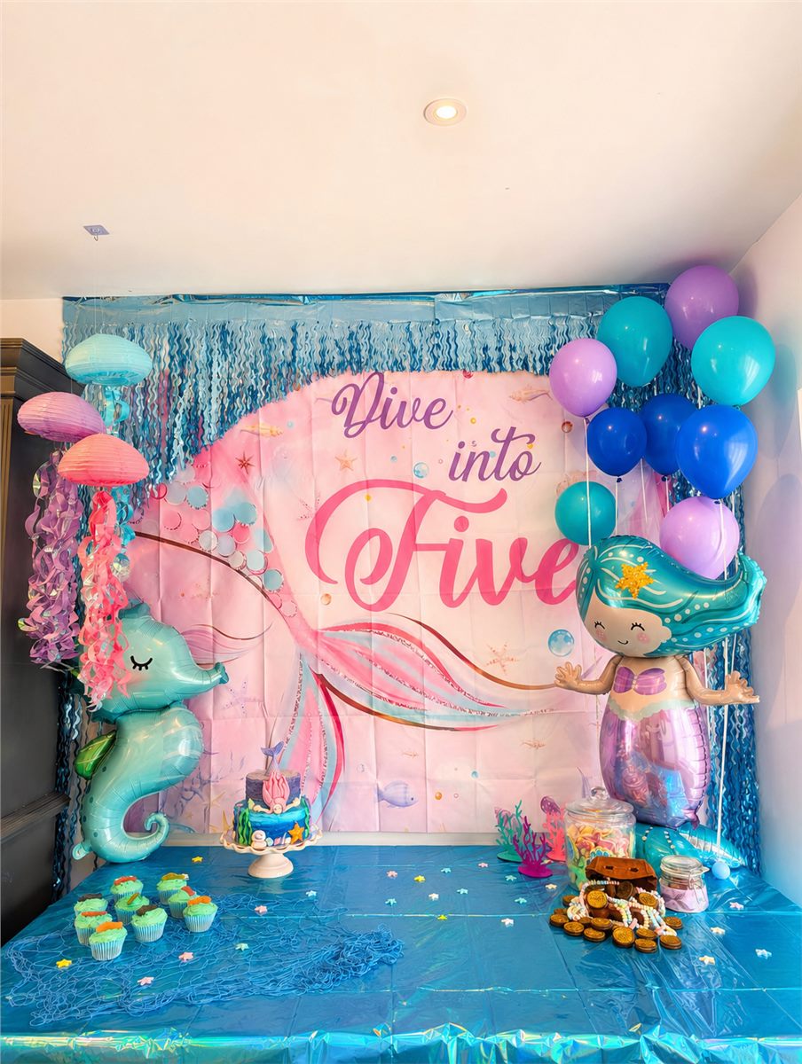Mermaid themed fifth birthday party backdrop with blue floor styling and colourful balloons.