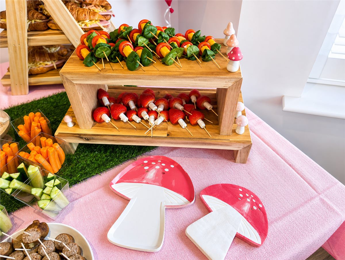 Woodland themed party food table with fruit, vegetables, croissants, and mushroom decorations.