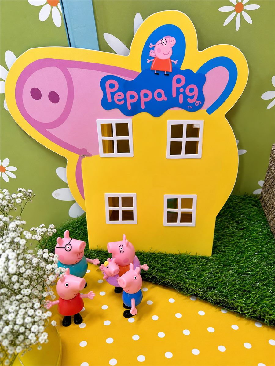 Peppa Pig themed party sign and small character decorations on a green daisy backdrop.